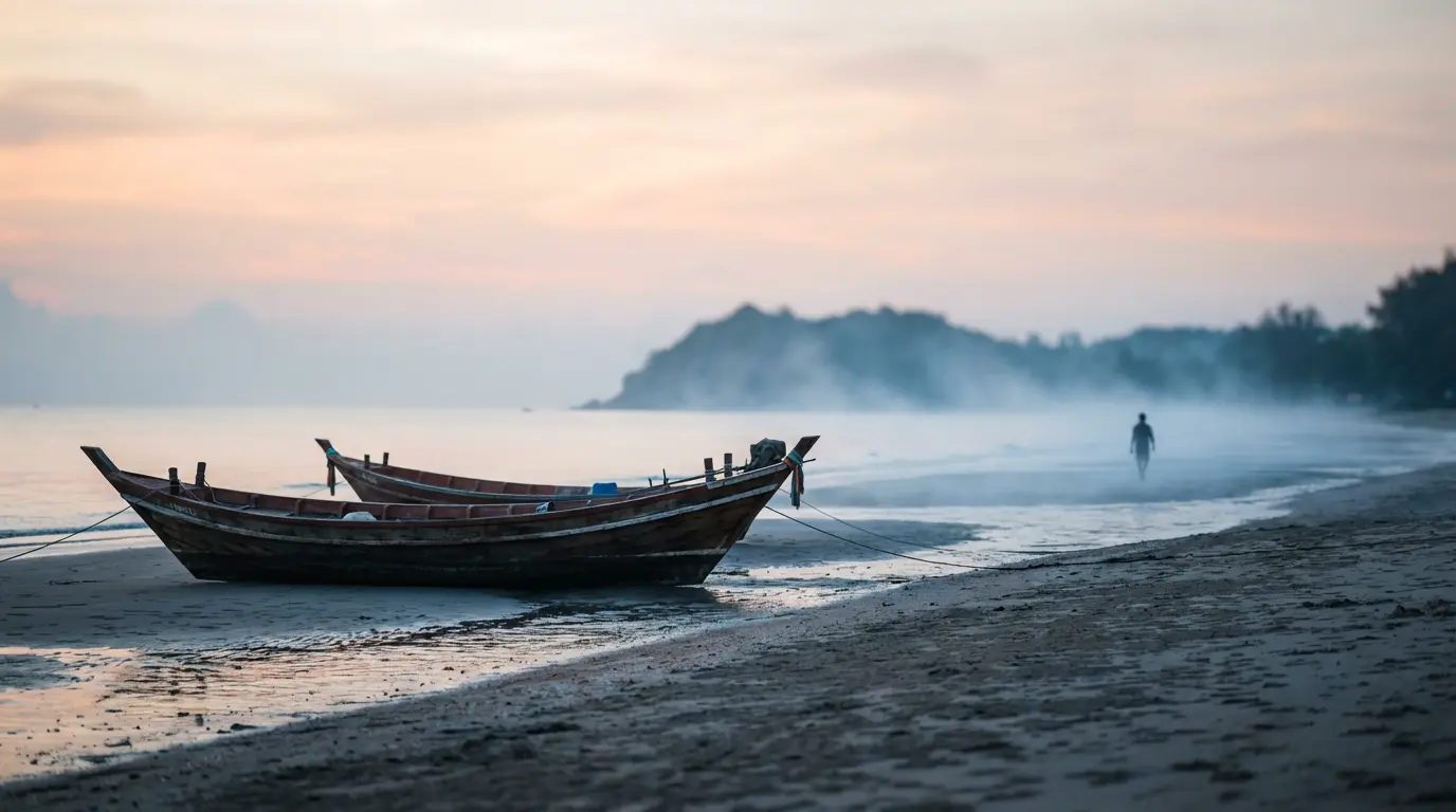 Quiet morning beach at the local end of Hua Hin with two empty longtail boats pulled up on damp sand and soft mist