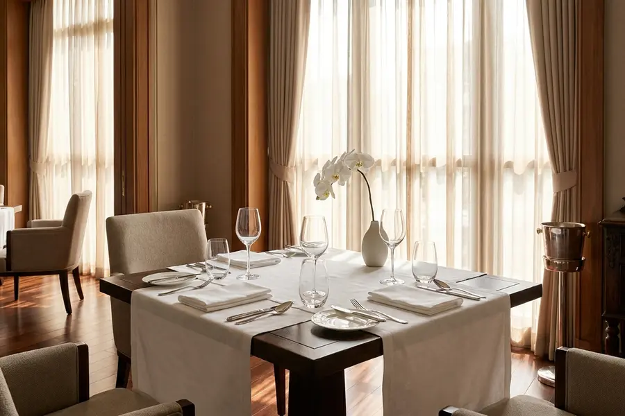 A polished private dining room in central Bangkok at midday with a single round table set for four and soft daylight from a tall window