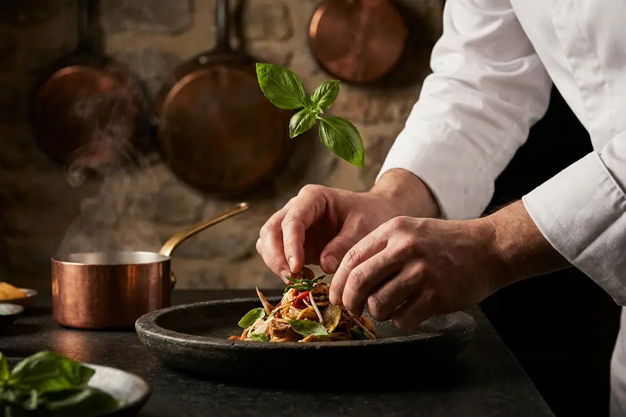 A clean villa kitchen island at midday with a basket of fresh herbs, a single chef's knife on a wooden board and soft daylight from a tall window