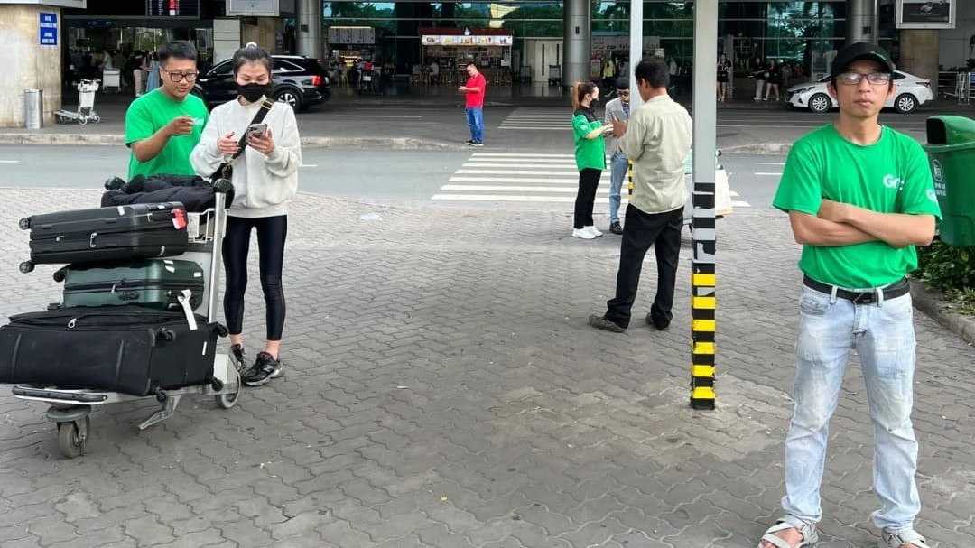 穿着 Grab 绿色制服的司机在新山一机场出境大厅外等候旅客，旁边有旅客拖着行李准备上车 / Win Royal Spa 皇家越式按摩