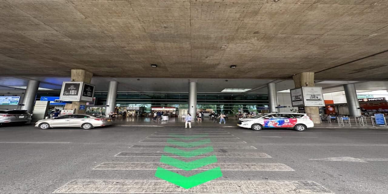 胡志明市新山一机场（SGN）出境大厅外的交通接送区，地面有 Grab 指示箭头，旅客拖着行李等候叫车 / Win Royal Spa 皇家越式按摩