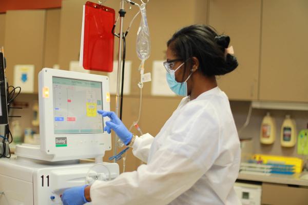 A dark-skinned female healthcare worker uses the dialysis machine.
