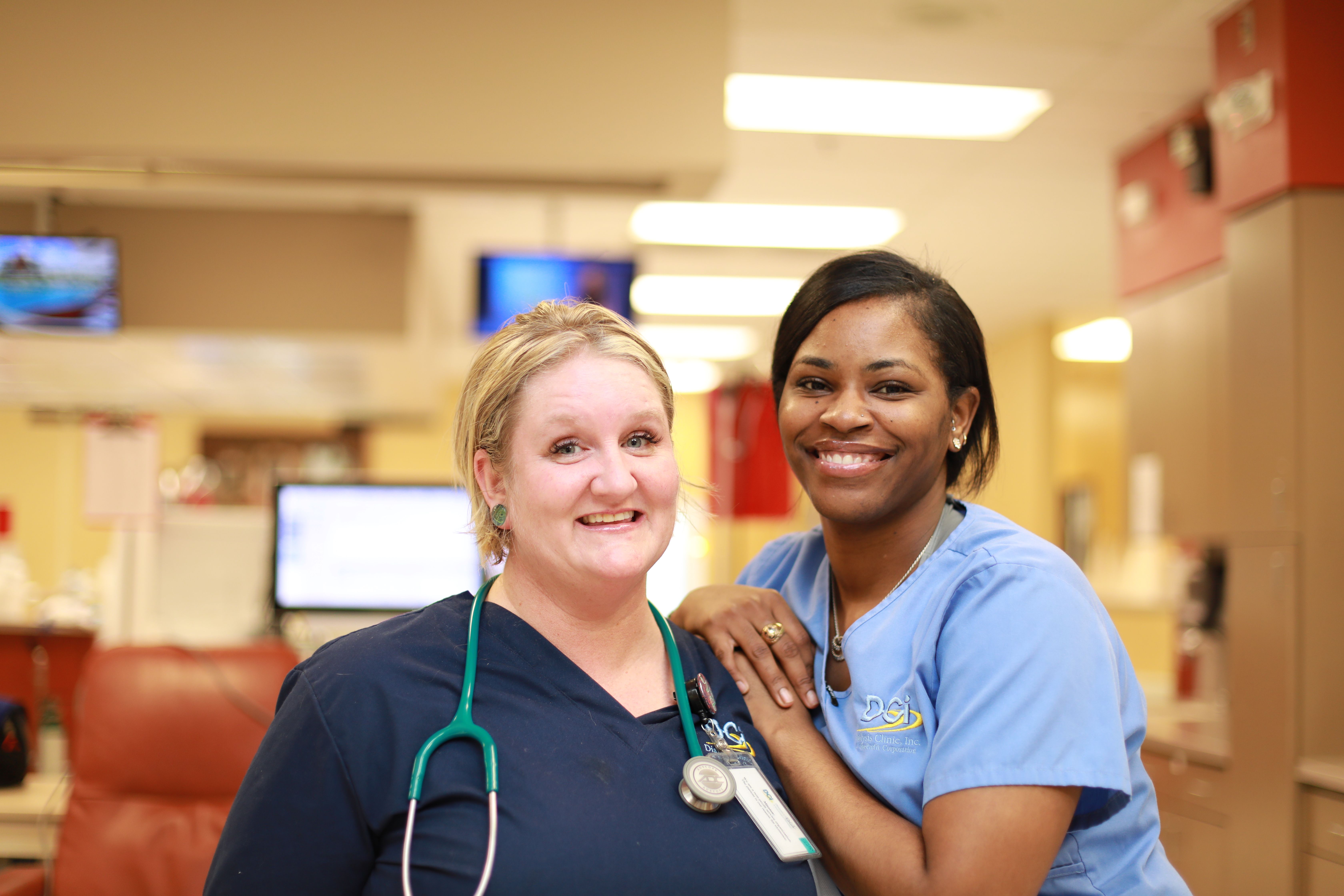 Two female healthcare workers, one white and one black, stand close together smiling.