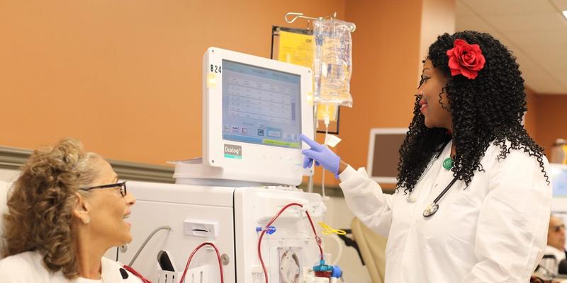 An older white female patient receives services with a black female dialysis nurse. 