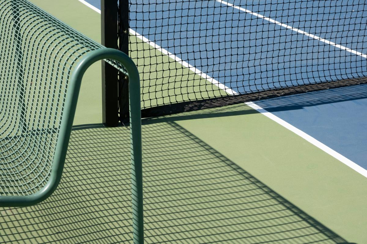 Outdoor court with a regulation net and bench in sunlight — the durable-goods side of a venue fitout that gets bought once