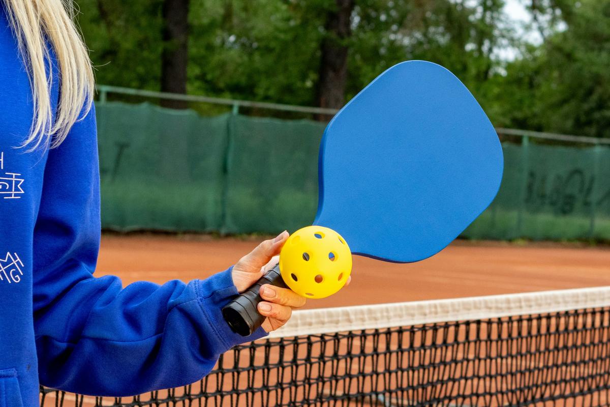 Hyper-realistic commercial product photography, a premium pickleball paddle resting on a sleek dark slate surface beside precision measurement tools including a digital caliper and a small weight scale, dramatic studio lighting with soft rim light highlighting the paddle edge guard and textured carbon fiber face, shallow depth of field, professional B2B e-commerce aesthetic, no text, no brand logo