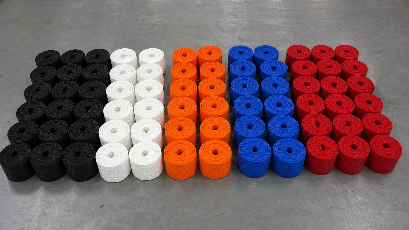 Rolled polyurethane pickleball grip wraps sorted into black, white, orange, blue and red colour groups on a factory table