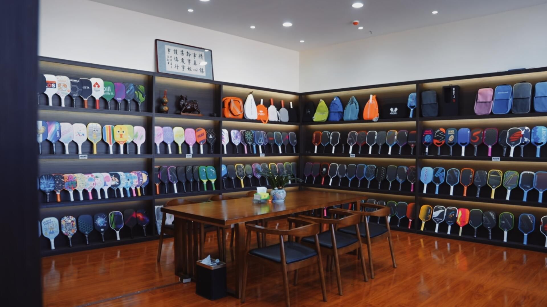 Showroom wall displaying dozens of pickleball paddle models in rows, each a separate SKU requiring its own model designation and certification record