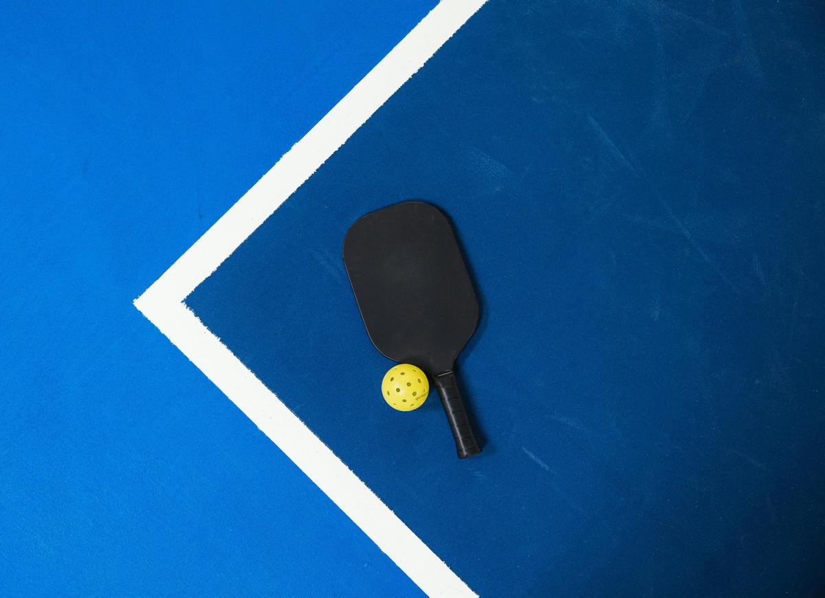 Hyper-realistic product photography, a small neat arrangement of six graphite pickleball paddles in different color finishes displayed on a minimal marble surface, compact low-volume wholesale concept, soft diffused natural window light, clean minimalist composition, elegant premium B2B product showcase aesthetic, no text, no brand logo