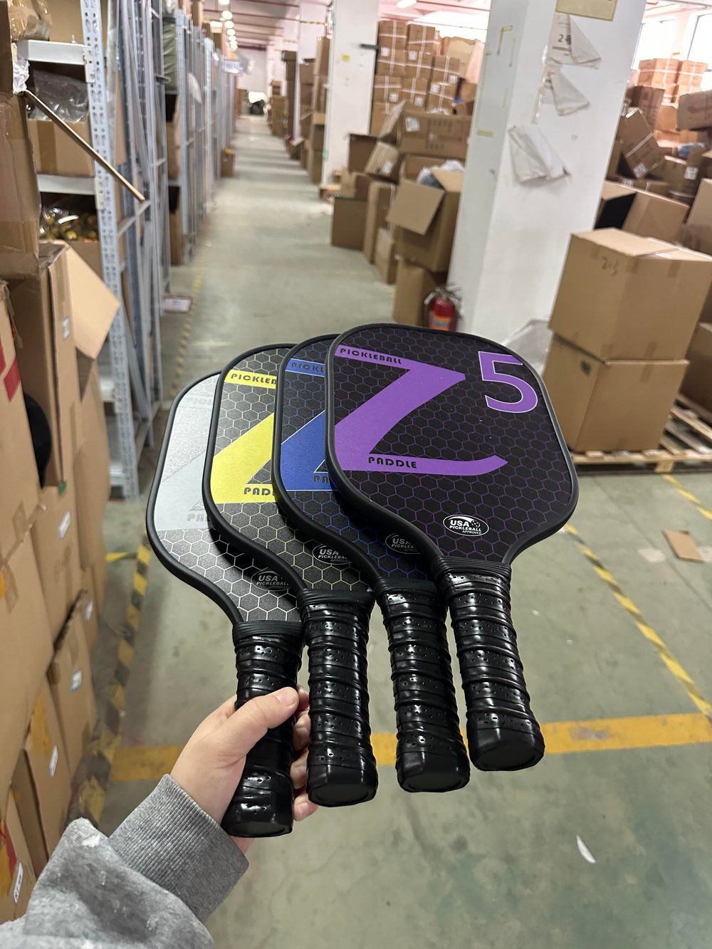 Four carbon pickleball paddles held by their handles showing grip and balance point at the handle end