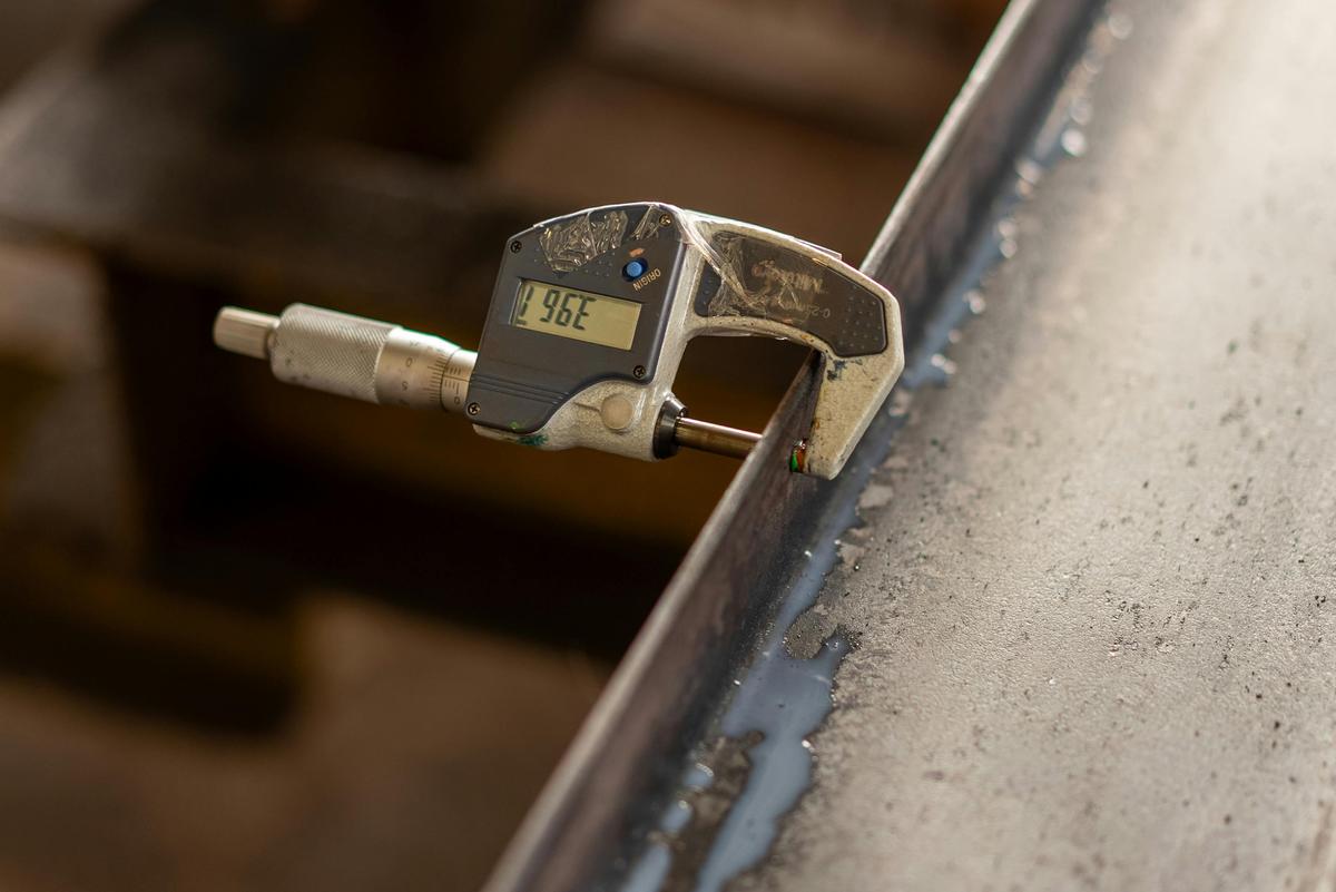 Hyper-realistic macro photography, a digital caliper measuring the thickness of a pickleball paddle edge guard on a precision inspection table, QC testing environment, focused spotlight on the measuring tool, blurred factory background, no text, no brand logo