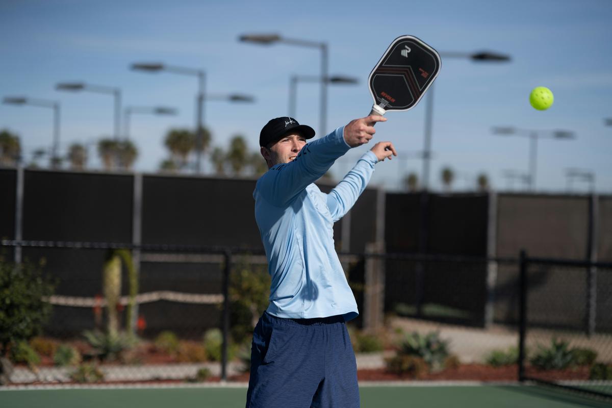 Hyper-realistic product photography, a premium graphite pickleball paddle resting on a sleek dark surface, surrounded by scattered digital error code projections and glitching holographic data streams, moody dramatic studio lighting with cool blue and warm amber accents, shallow depth of field, high-end commercial sports equipment aesthetic, no text, no brand logo