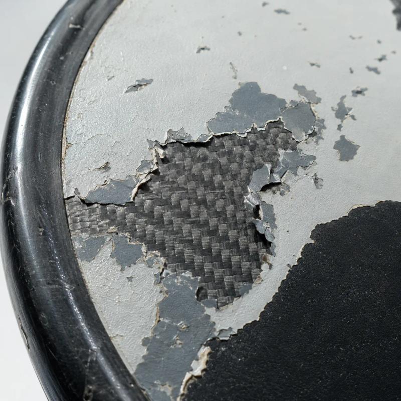Macro of a pickleball paddle face where a grey coating has flaked away in patches, exposing the woven carbon fibre underneath