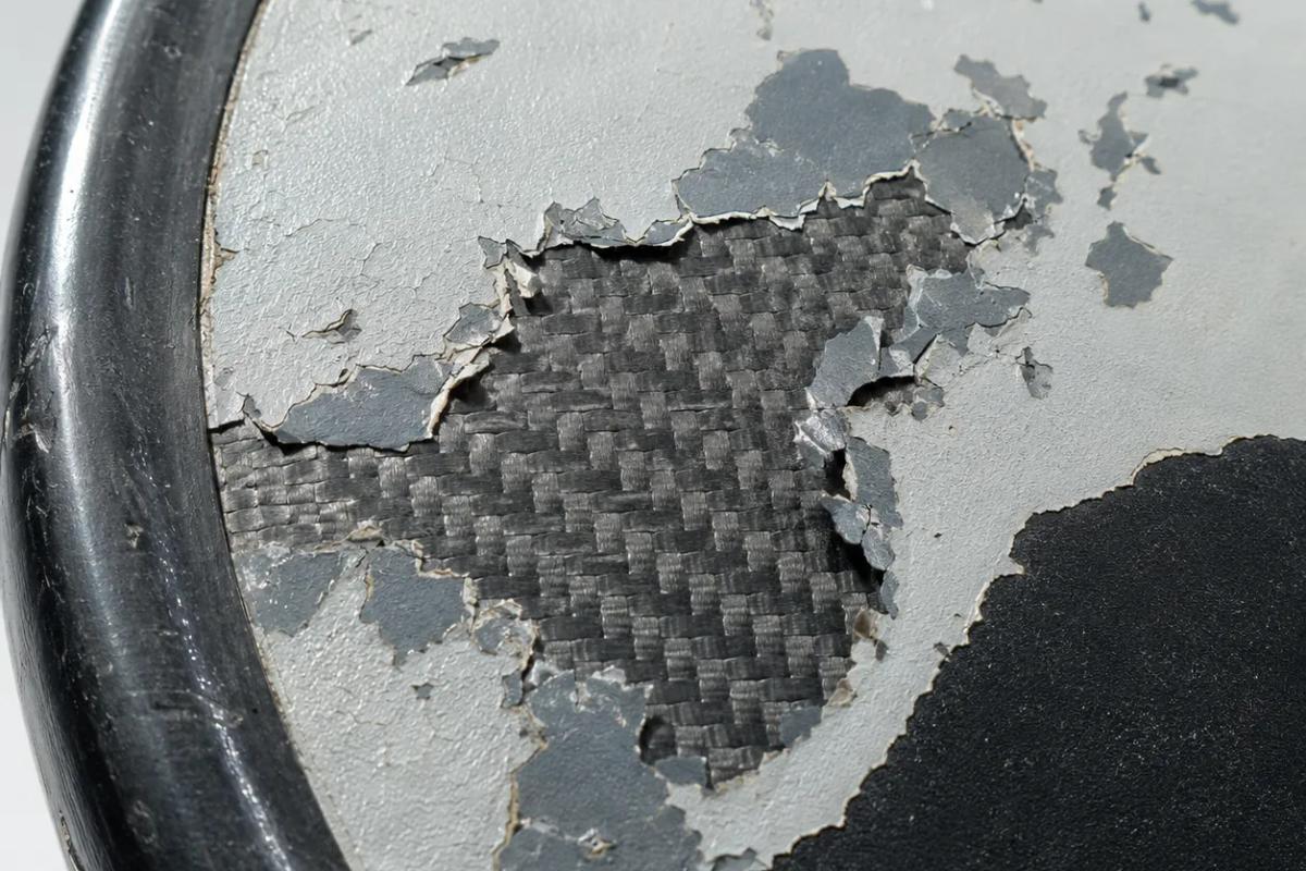 Macro of a pickleball paddle face where a grey coating has flaked away in patches, exposing the woven carbon fibre underneath