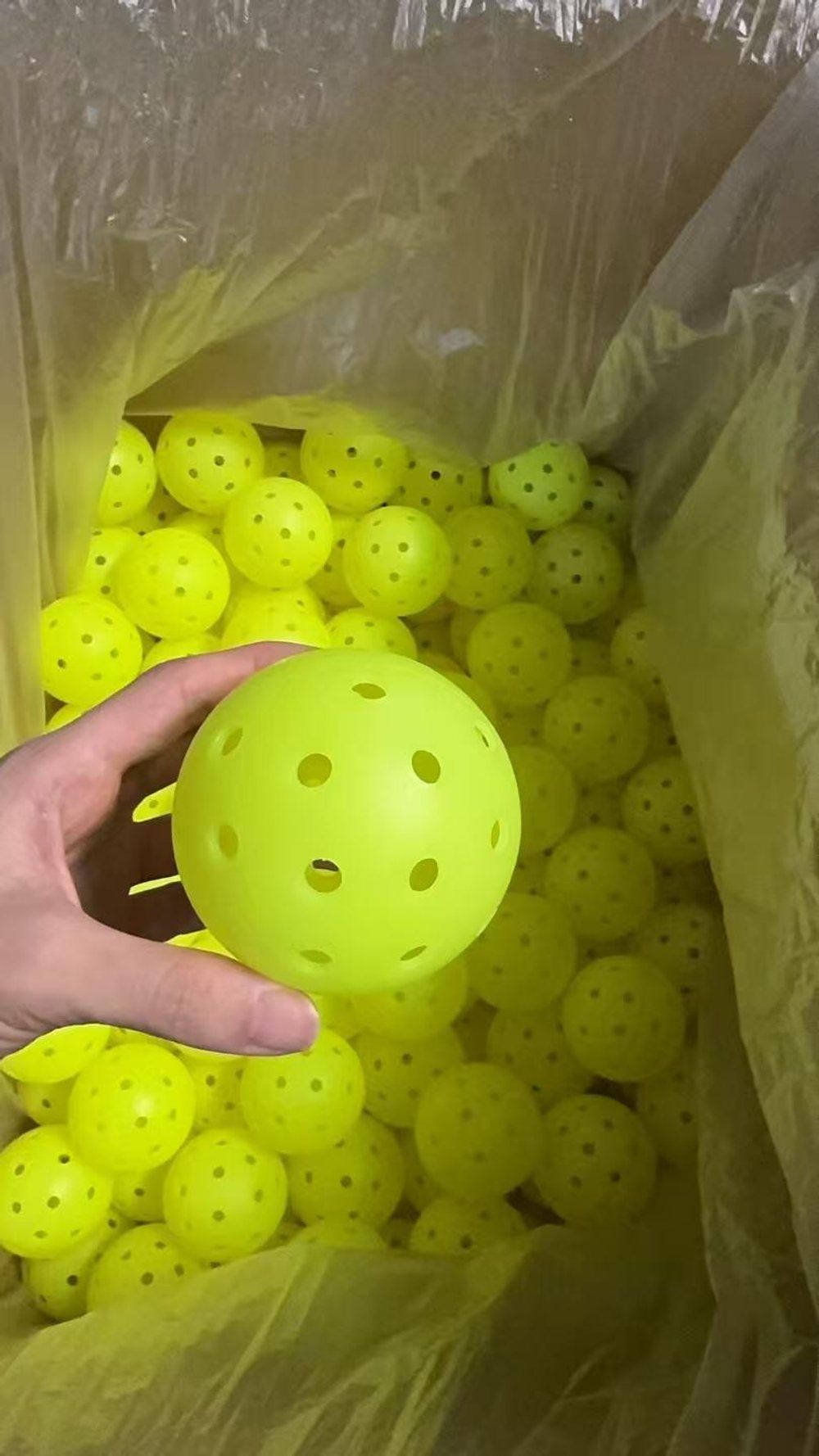 Inspector checking a 40-hole pickleball from a sampled batch for roundness, holes and surface defects