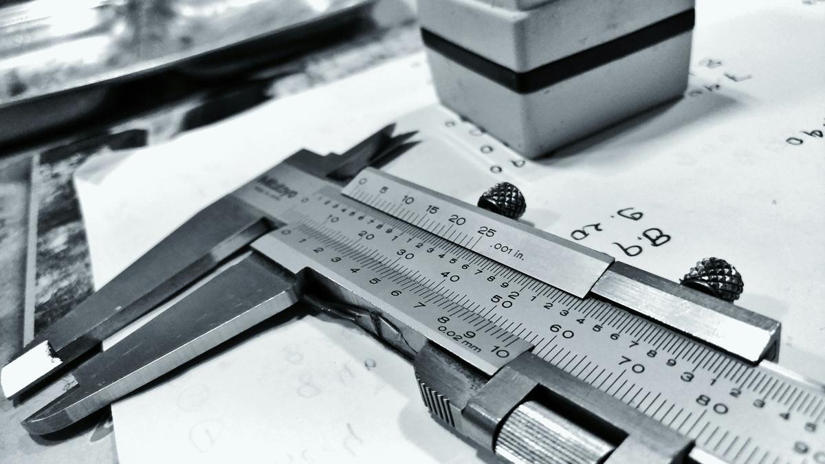 Hyper-realistic product photography, a pair of digital calipers measuring the exact grip diameter and edge guard thickness of a premium pickleball paddle on a sterile steel inspection table, dramatic studio lighting emphasizing precision and quality control, highly detailed texture, clean composition, no text, no brand logo