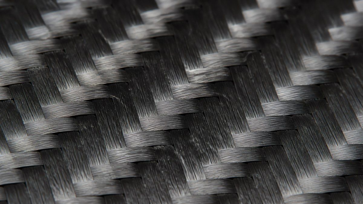 Extreme macro of a 12K two-by-two twill carbon fabric showing wide flattened tows forming broad diagonal ribs