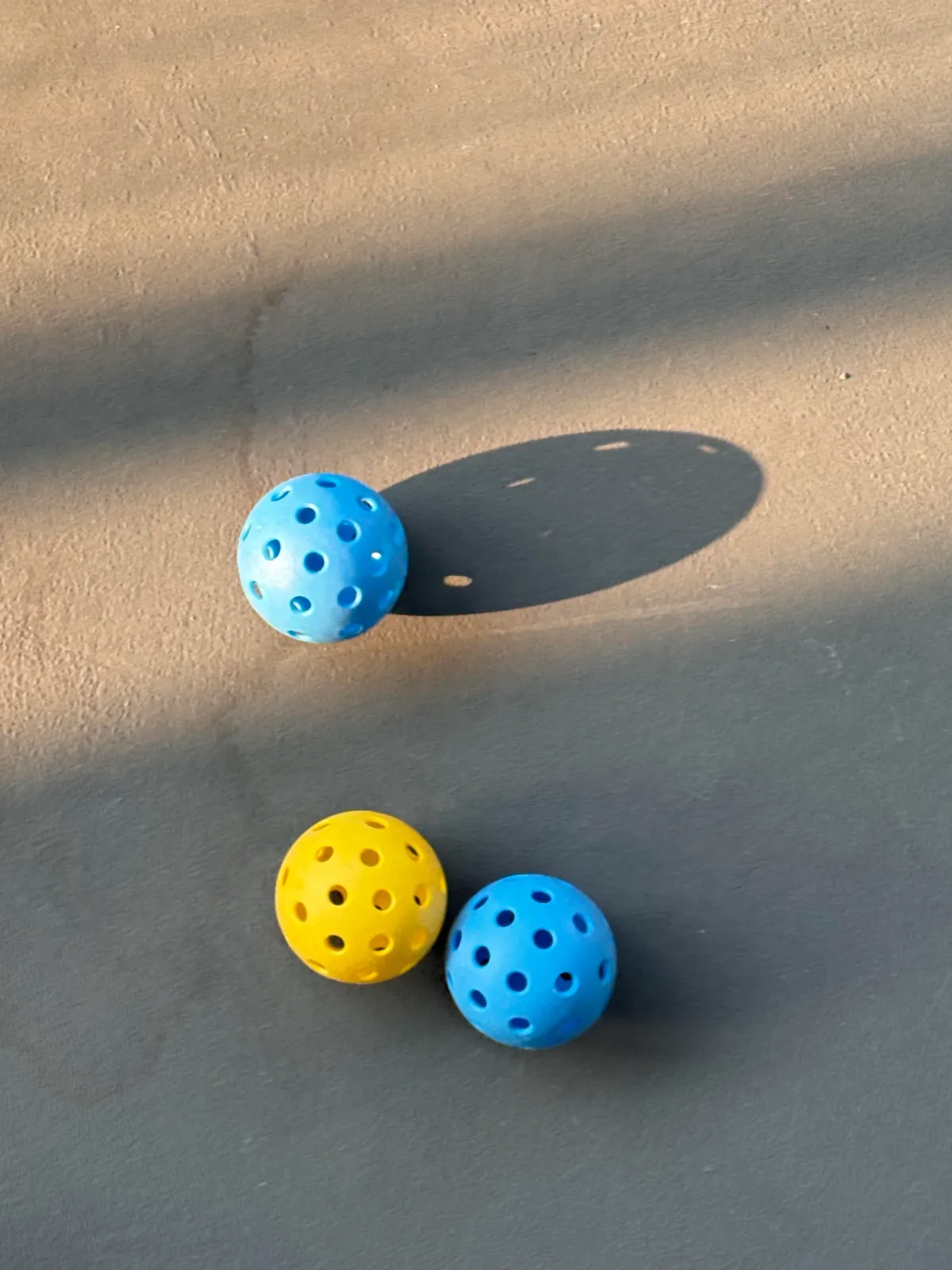 Three loose yellow and blue perforated balls on a court surface