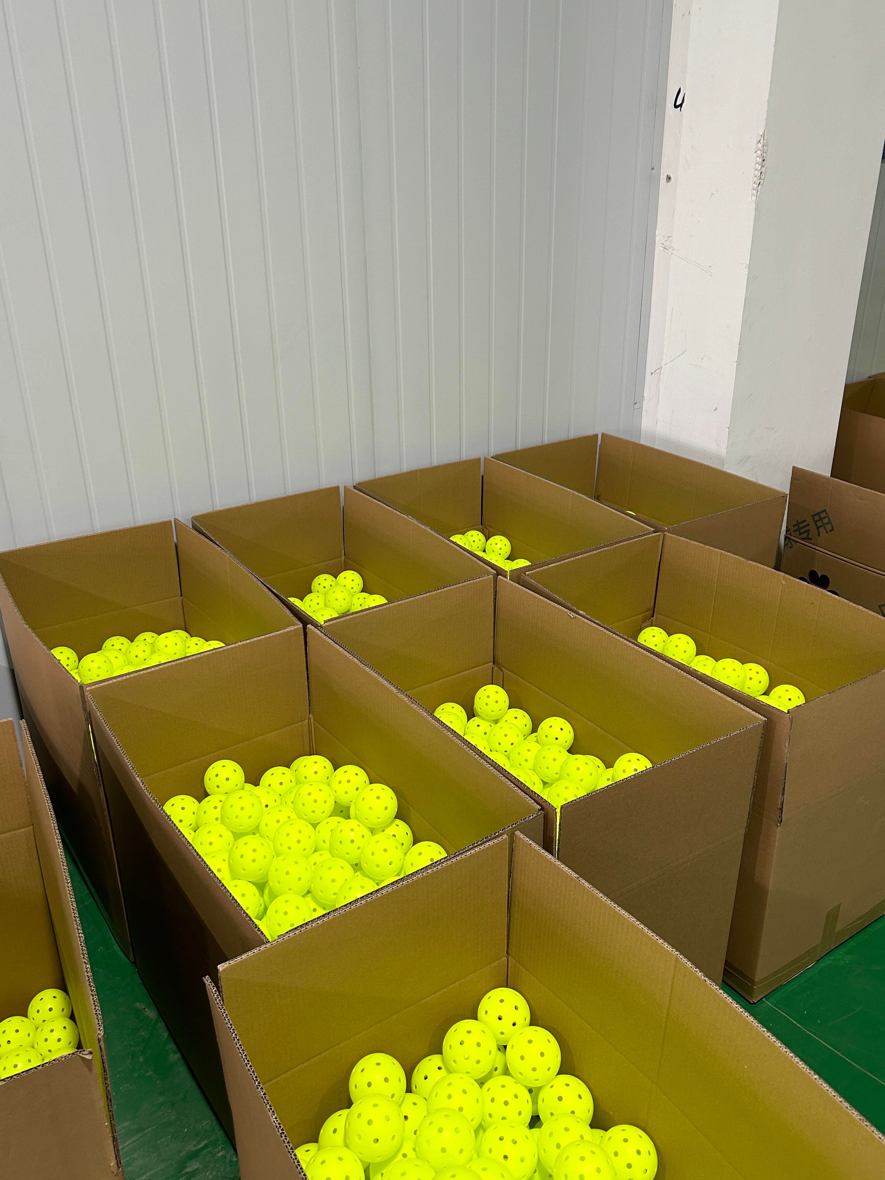 Cartons of neon pickleballs staged at a factory, the point where a private-label color is set for a production run
