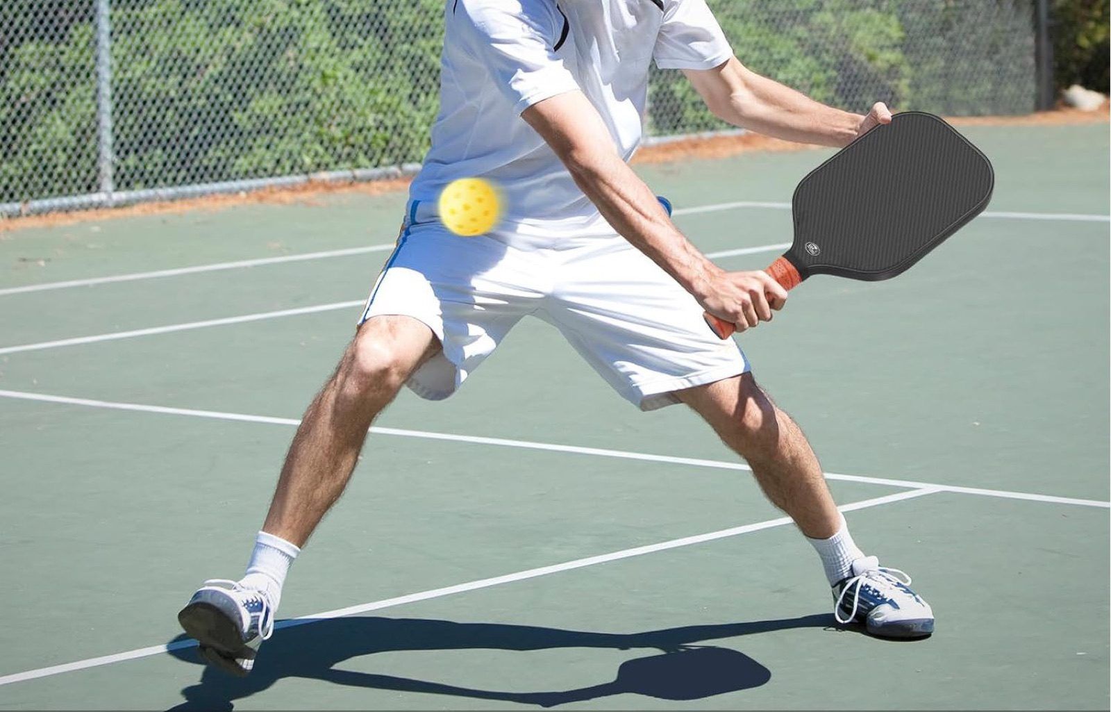 Player striking a pickleball with a raw carbon faced paddle on an outdoor court