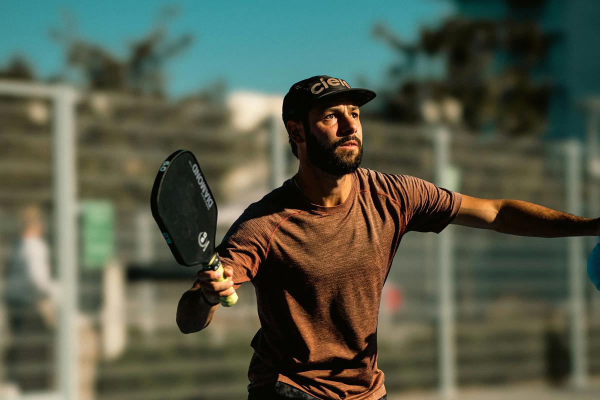 Hyper-realistic product photography, side-by-side comparison of two pickleball paddles on a neutral gray surface, one with perfect finish and one with warped face and loose edge guard, magnifying glass hovering over the defective area, clean minimalist composition, professional studio lighting, no text, no brand logo