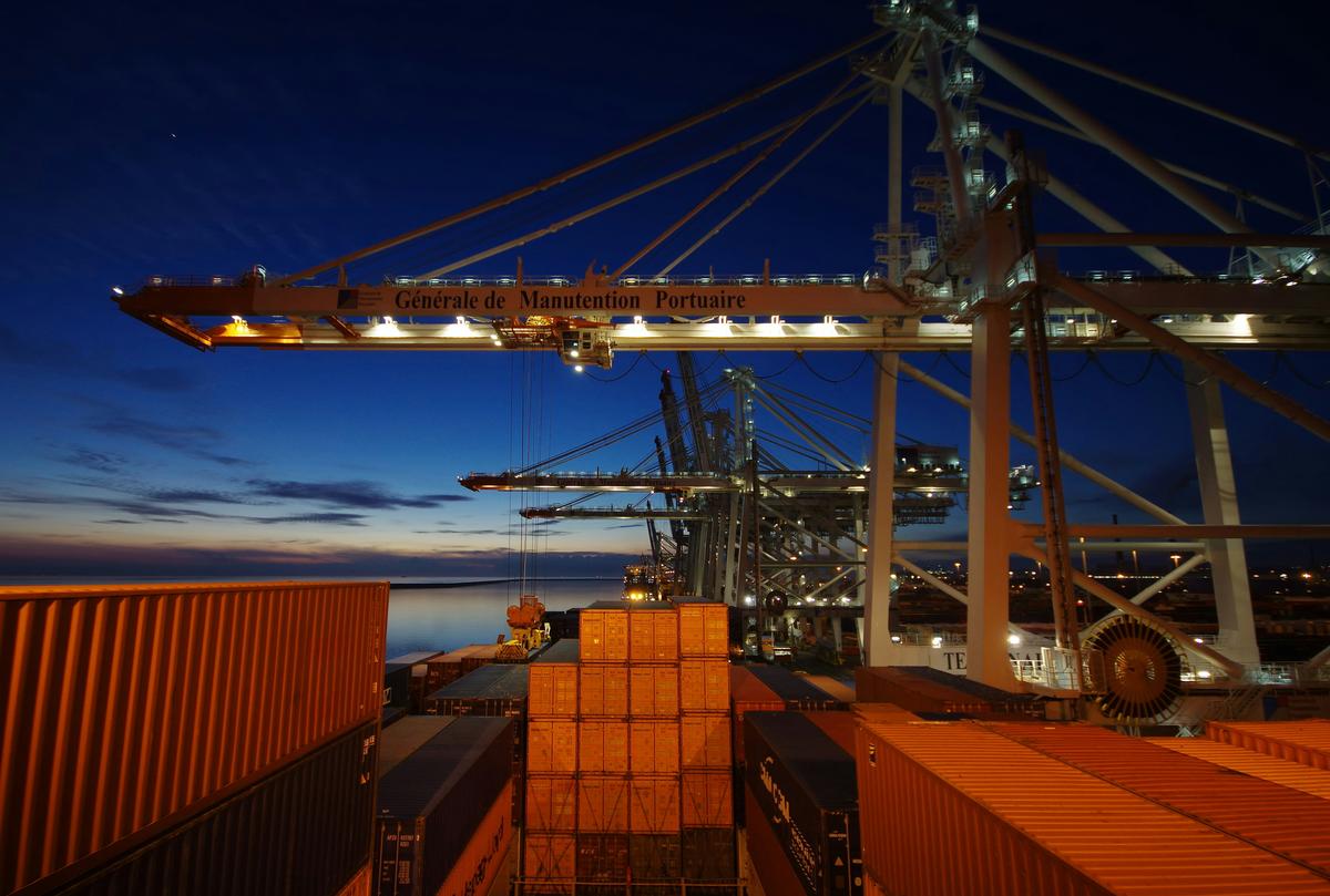 Hyper-realistic commercial photography, a sealed corrugated shipping container being loaded with palletized boxes of pickleball paddles by a container crane at a busy port terminal, golden hour sunlight casting long shadows, shipping containers stacked in the background, international trade logistics aesthetic, no text, no brand logo
