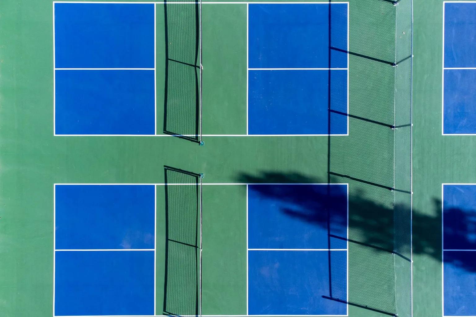 Top-down view of two pickleball courts with blue in-bounds acrylic colour coating, a green surround coating and white painted lines, the surfaced area extending well beyond the play lines