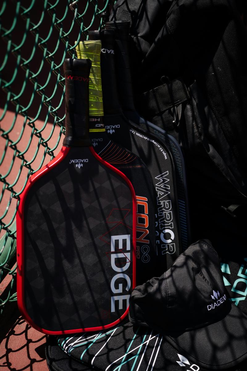 Hyper-realistic product photography, three pickleball paddles displayed side by side on a matte black surface each with a different minimalist graphic decal on the face representing distinct private label brand identities, subtle spotlight from above creating soft shadows, premium showcase presentation style, no text, no brand logo