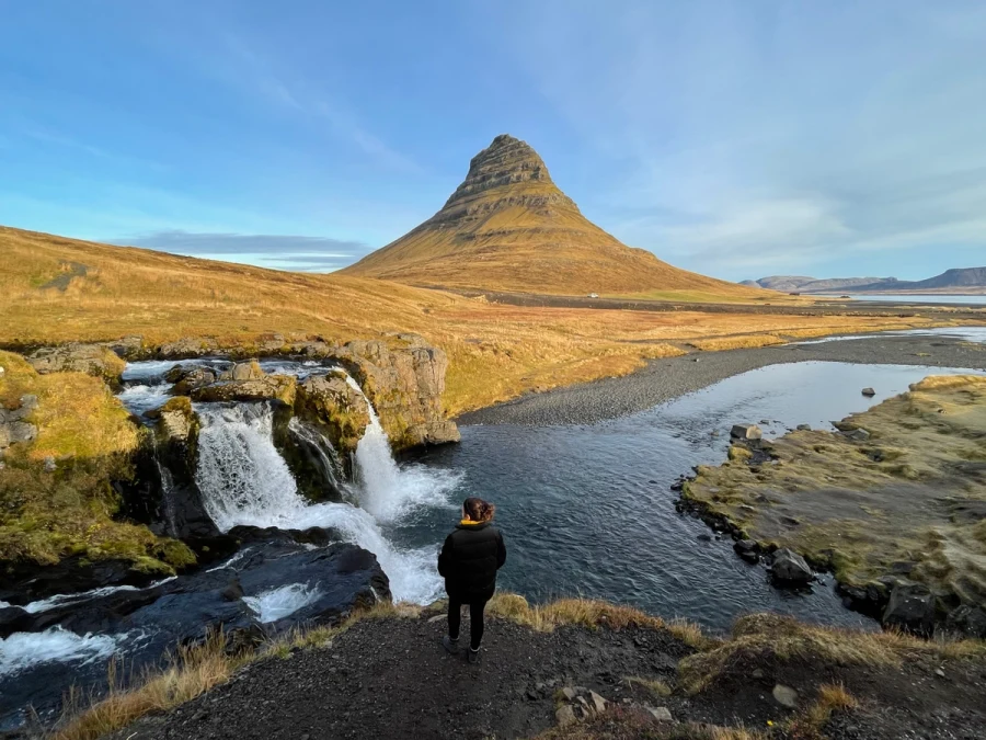 Kirkjufell mountain and Kirkjufellsfoss waterfall under a moving sky, a person standing at the falls