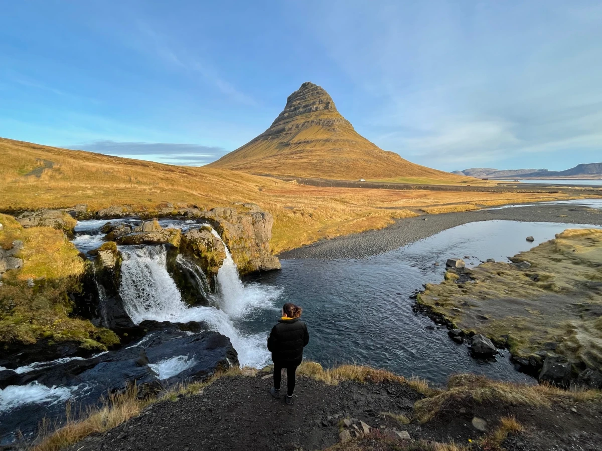 Kirkjufell mountain and Kirkjufellsfoss waterfall under a moving sky, a person standing at the falls
