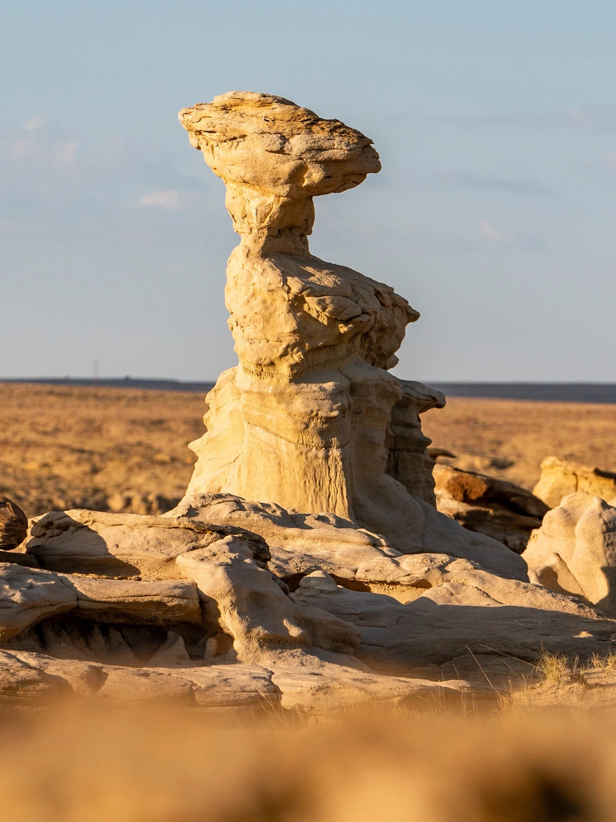 A single capped hoodoo catching low golden light, with the open plain stretching behind it