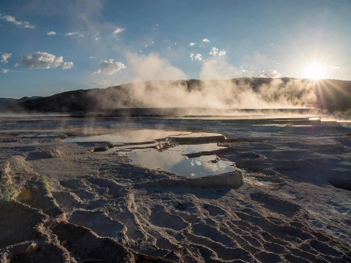 A sunstar bursts through rising steam over the reflecting travertine pools of Mammoth Hot Springs at Yellowstone