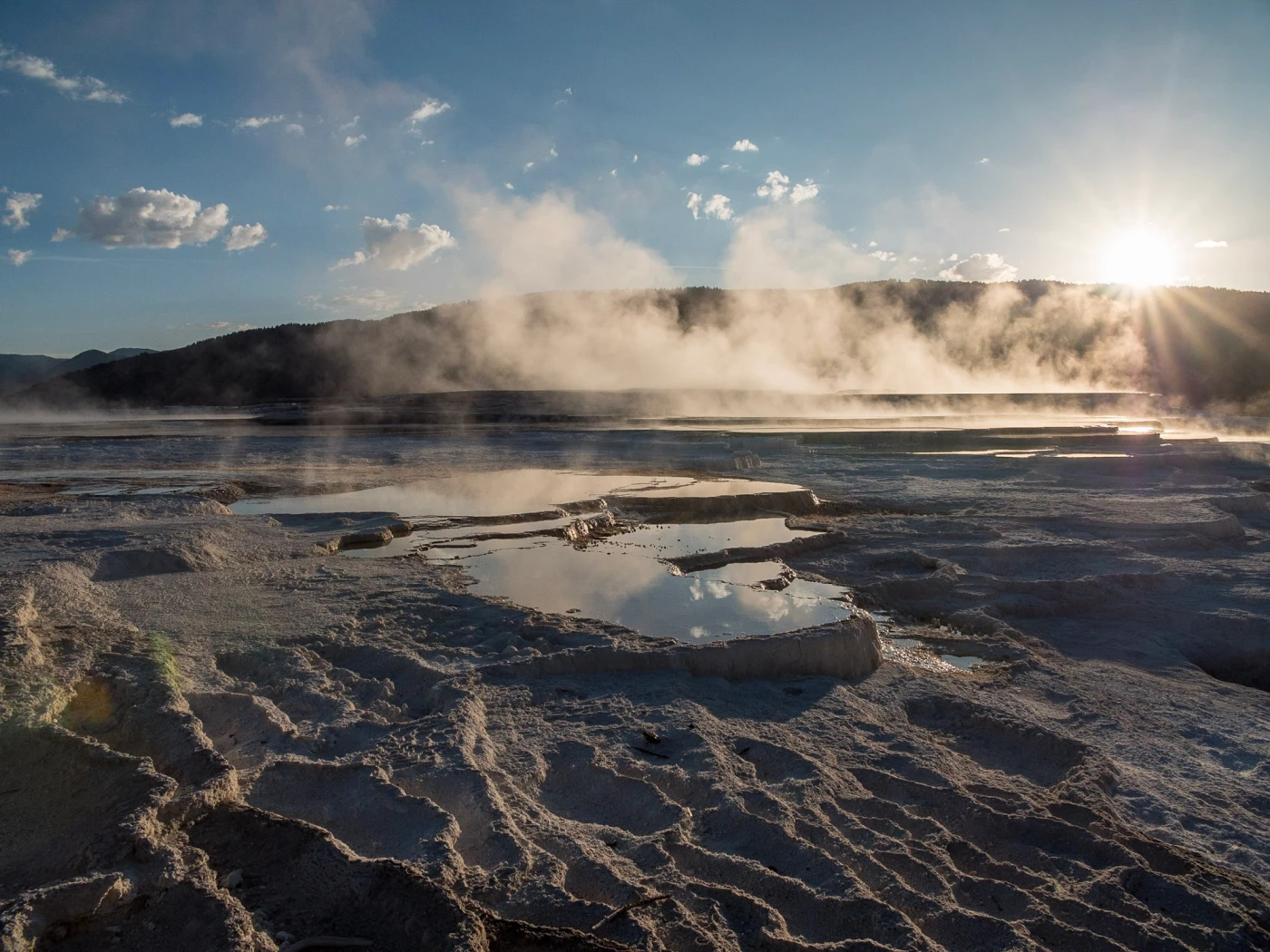 A sunstar bursts through rising steam over the reflecting travertine pools of Mammoth Hot Springs at Yellowstone