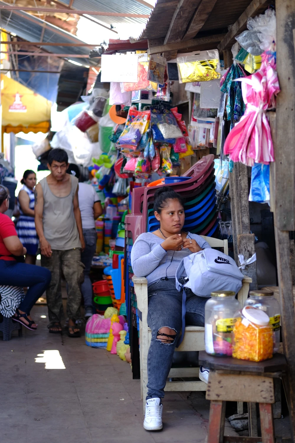 The crowded interior of Granada’s municipal market, stalls piled with toys and plastic goods, a vendor resting among them