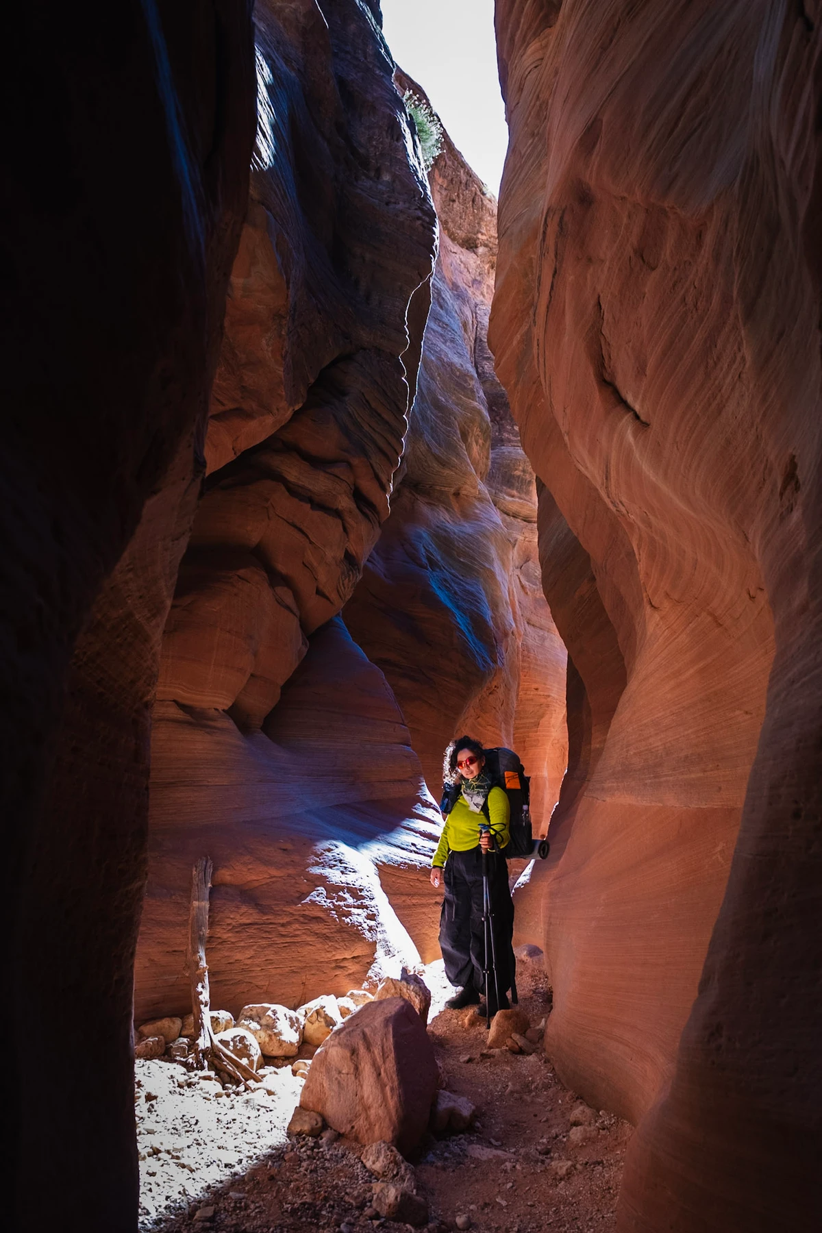 A backpacker standing in a sunbeam where the slot canyon pinches to shoulder width