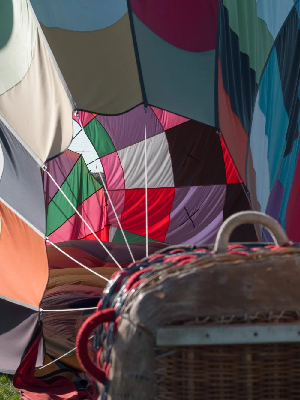 A close view into the colorful fabric panels of a hot-air balloon envelope with a wicker basket in the foreground