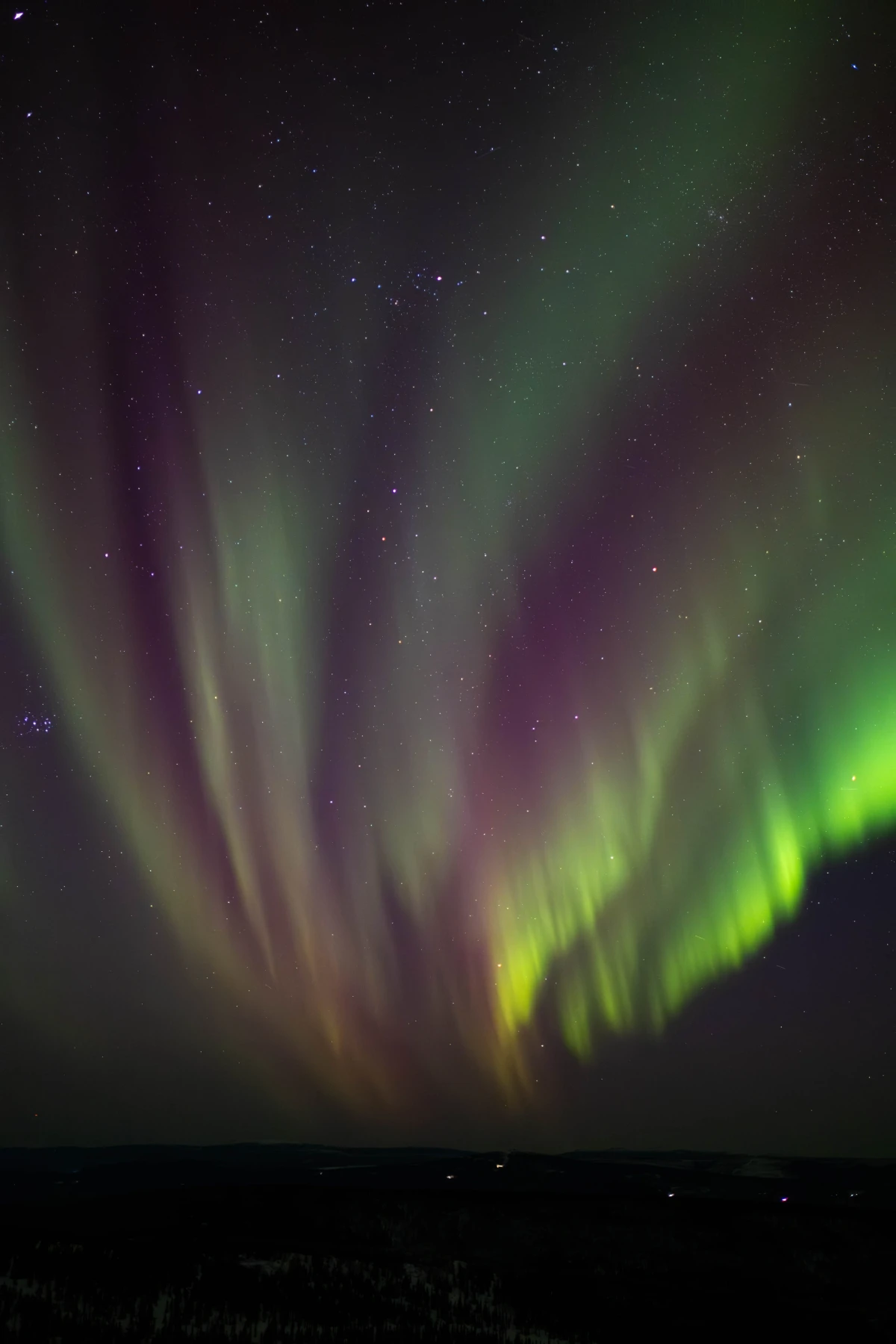 A full-sky aurora corona with green, purple, and yellow rays radiating overhead among the stars