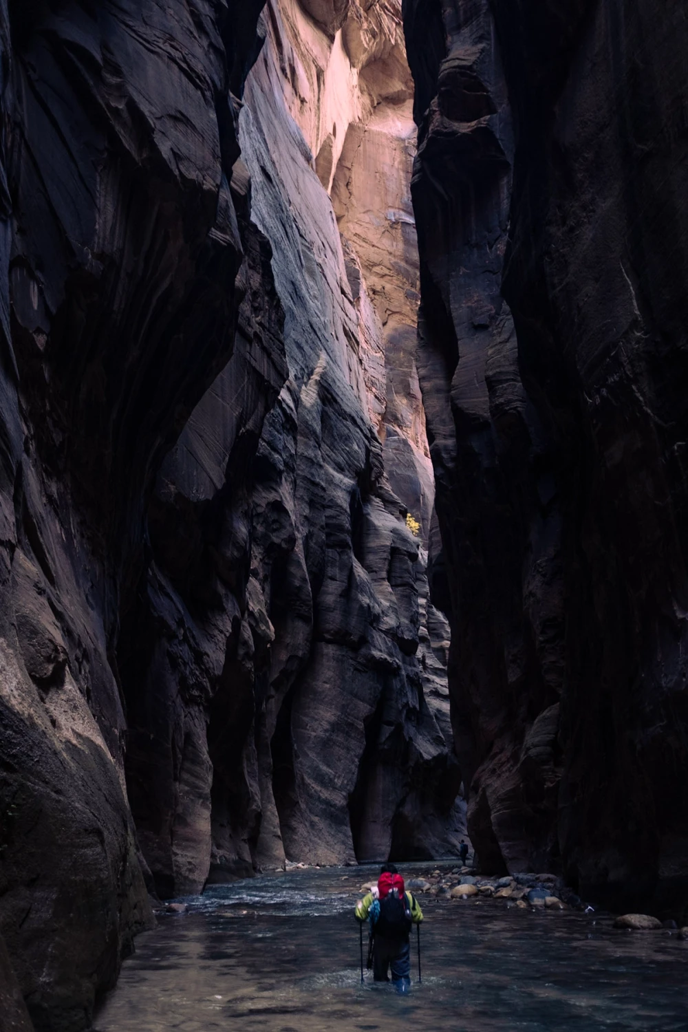 A hiker with a red pack wading through a column of light in the narrowest section