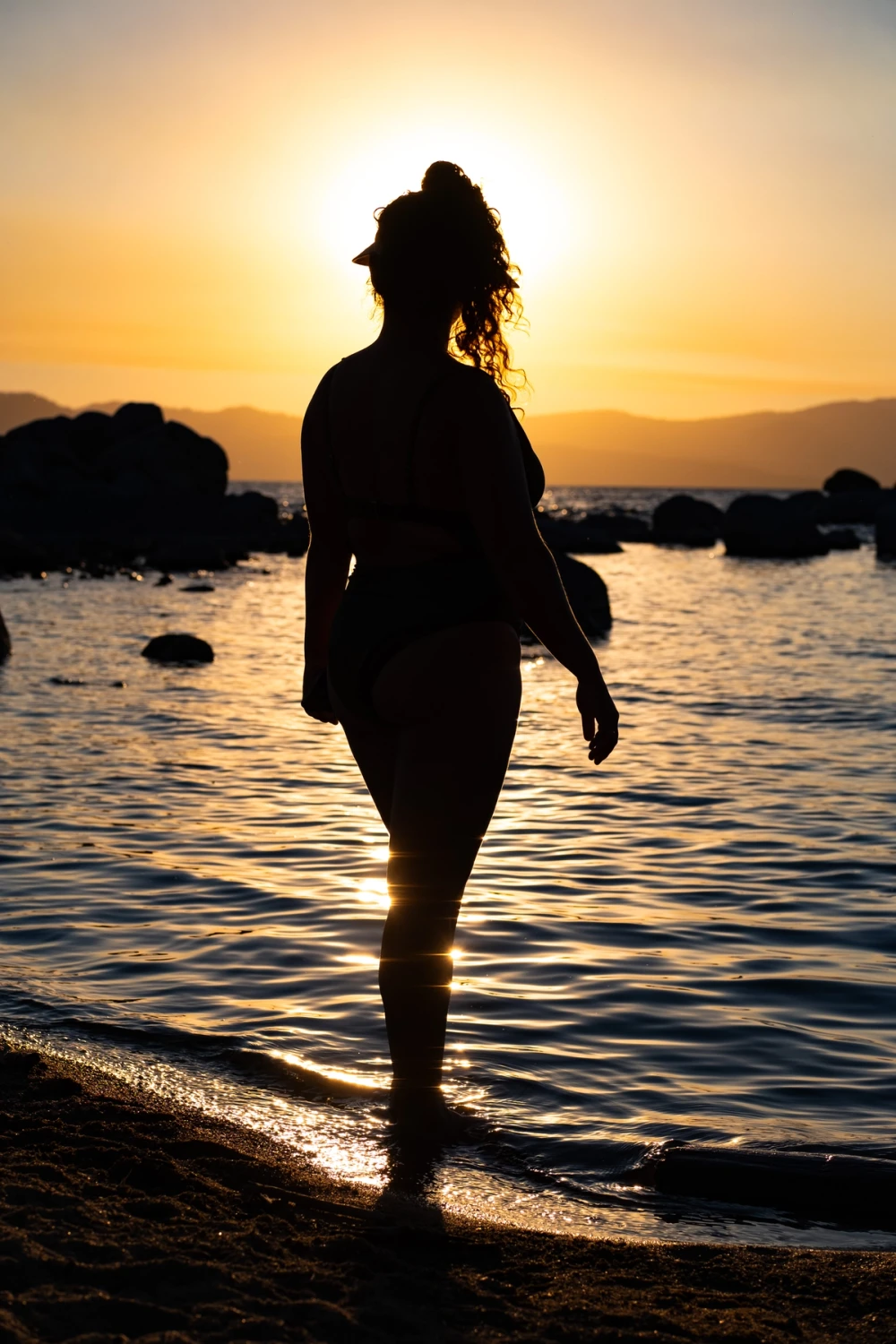 Silhouette of a person standing ankle-deep in Lake Tahoe at sunset, golden sky and far mountains behind
