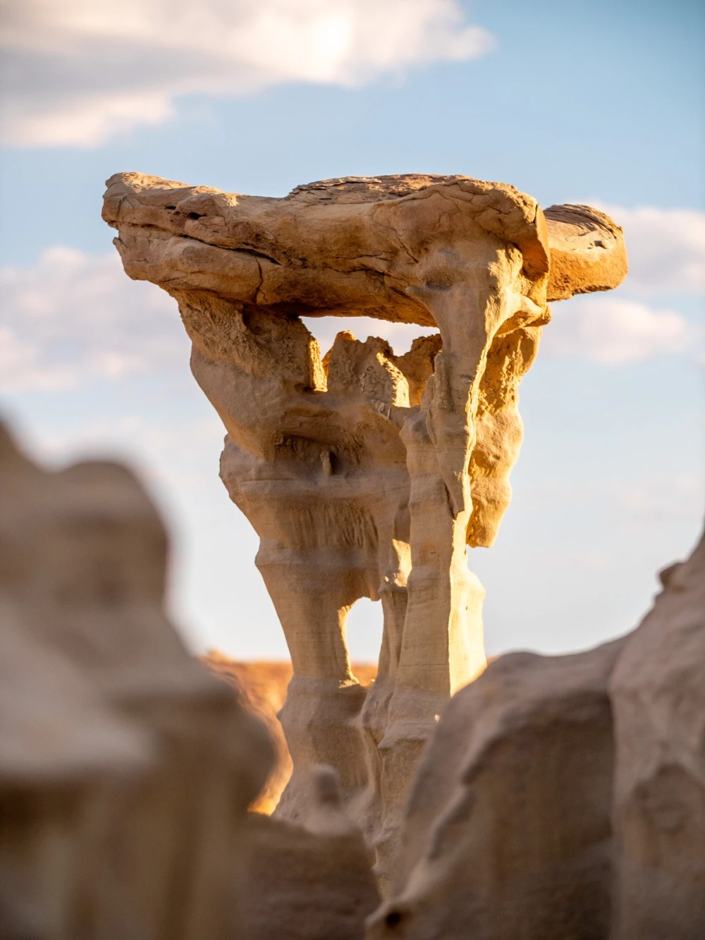A wide slab of caprock balanced on a thin sandstone pedestal, backlit by the sun