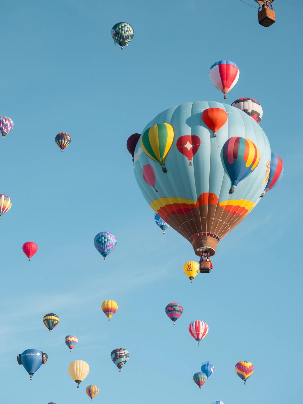 A sky full of drifting hot-air balloons, a balloon-print balloon and a yellow KOA balloon among them