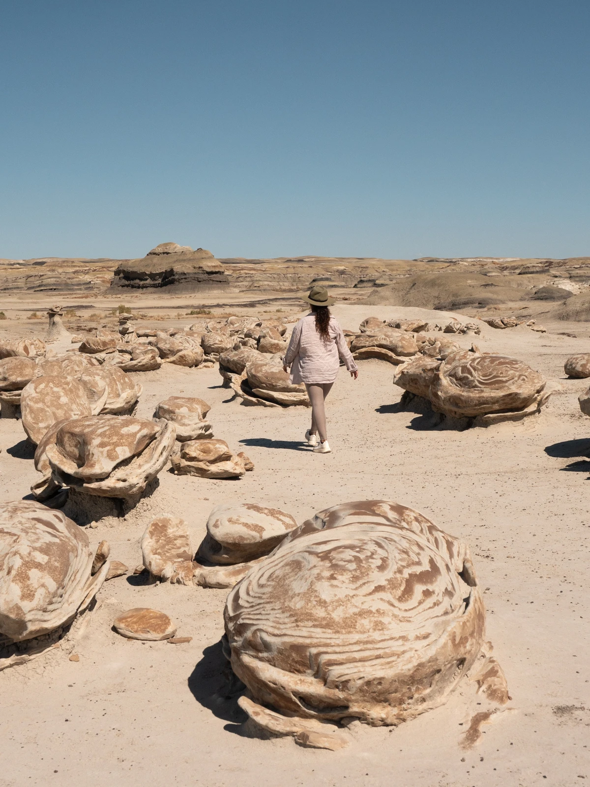 A person in a sun hat walking among rounded, cracked sandstone egg formations under a clear sky