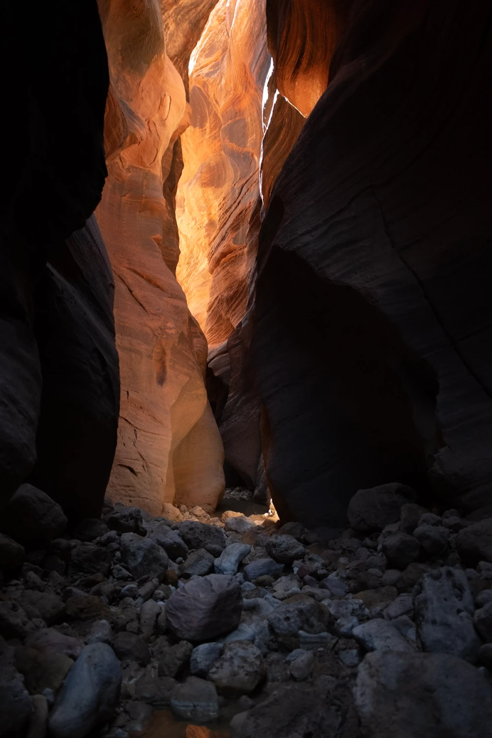 A jumble of boulders on the canyon floor below a glowing slot opening