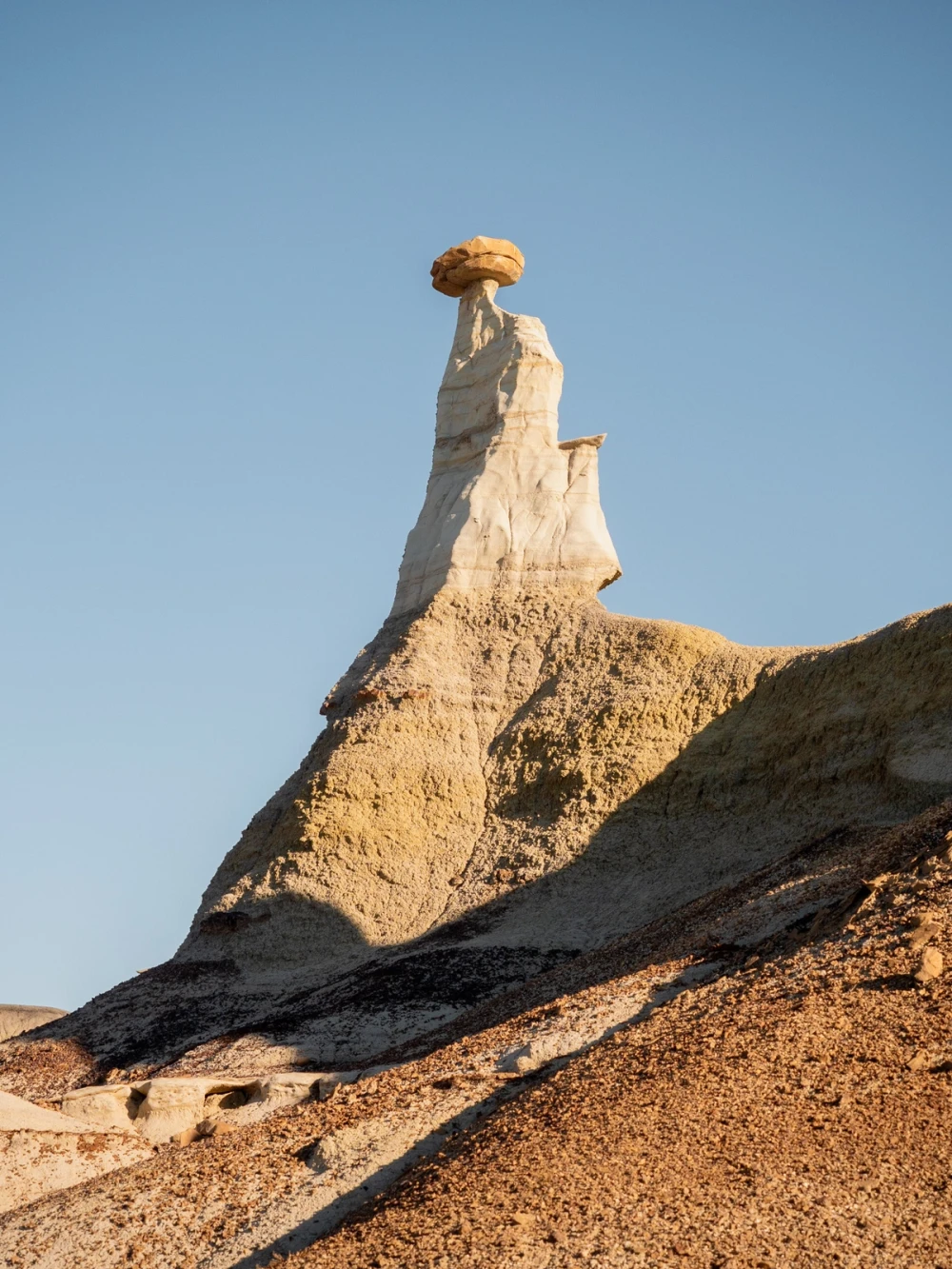 A capped spire rising from a striped clay slope against a clear blue sky
