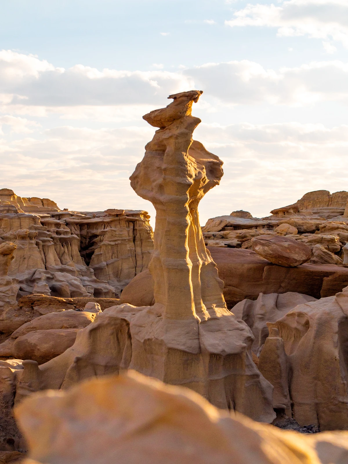 A slender sandstone spire backlit by the setting sun, ringed by eroded sandstone blocks