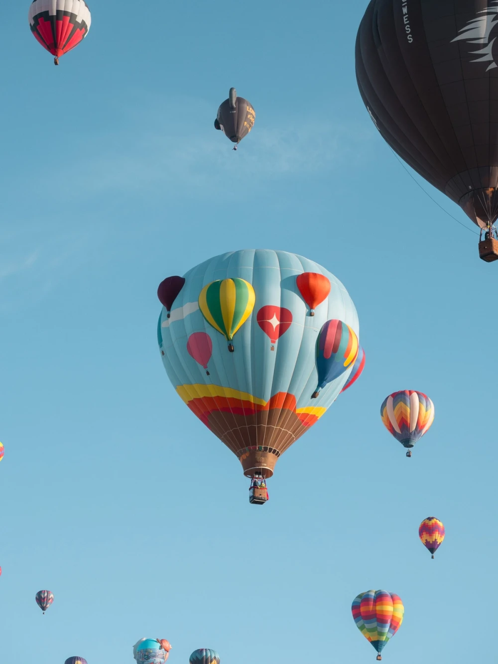 A pale blue hot-air balloon decorated with painted hot-air balloons drifting among many others in a blue sky