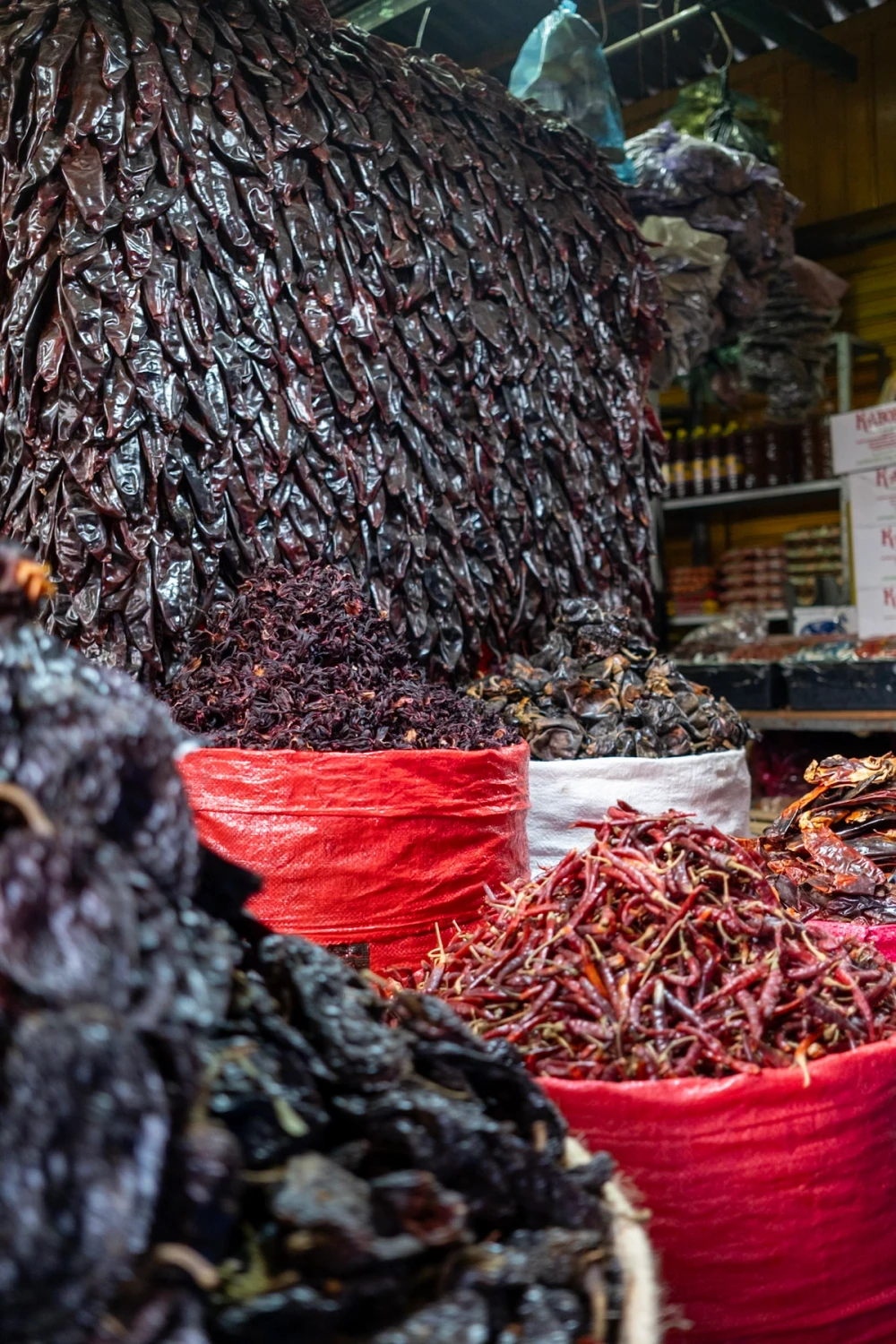 A market stall piled high with mounds of dark dried chiles, some spilling from large red woven sacks