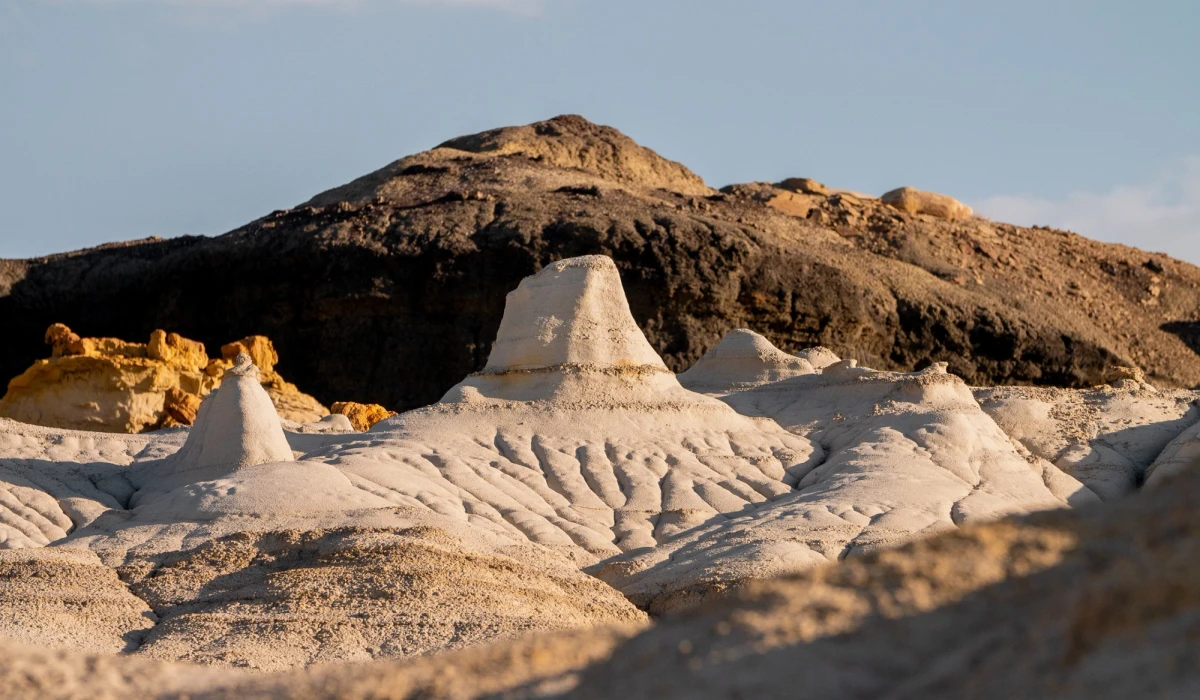Pale sandstone mounds glowing in golden light beneath a dark caprock hill at Bisti Badlands
