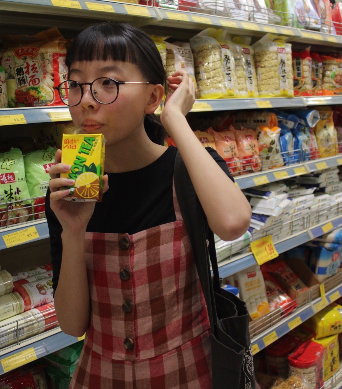 A person in a supermarket drinking a box of lemon tea. 