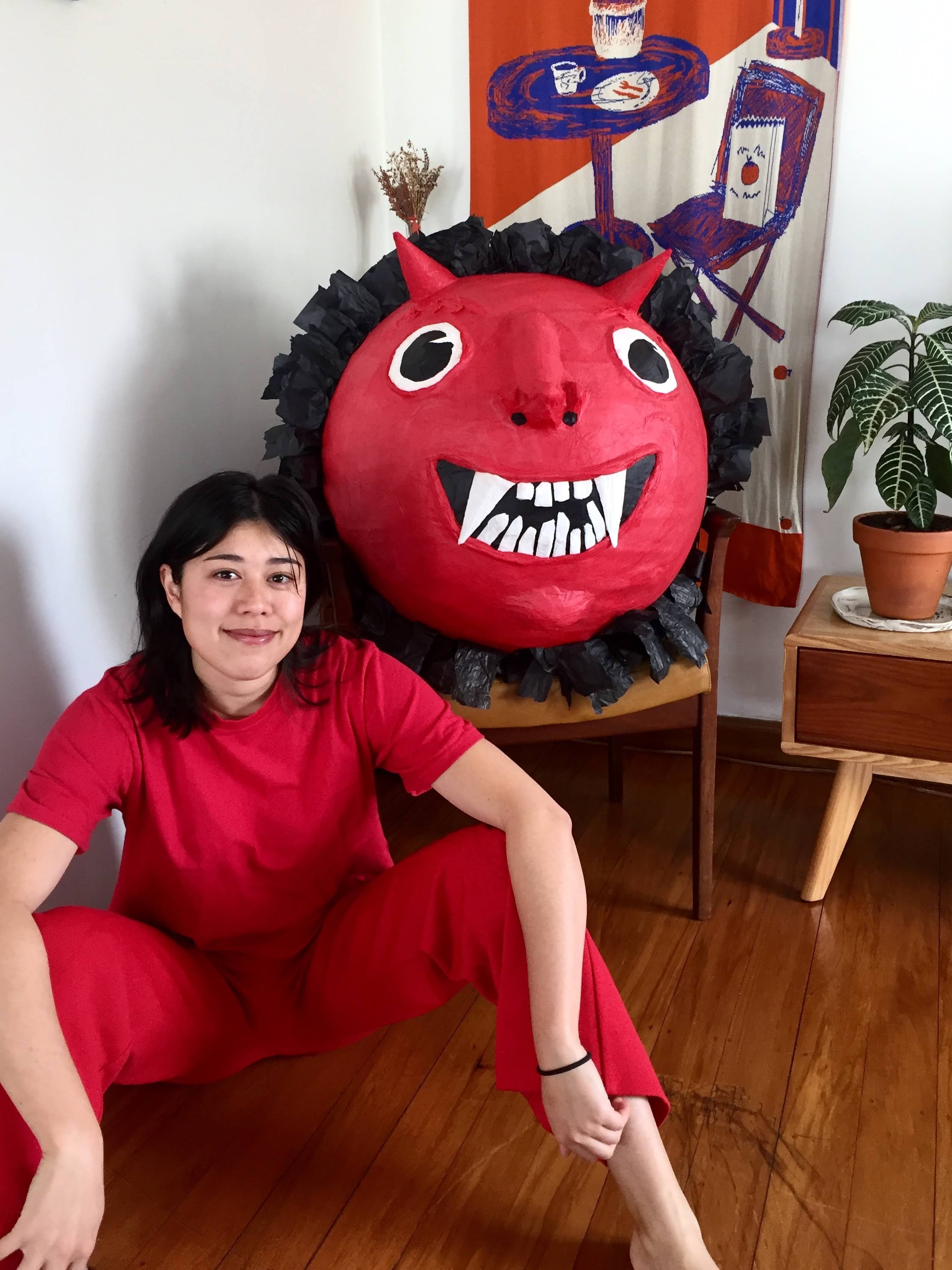 A woman in red standing next to a friendly demon piñata